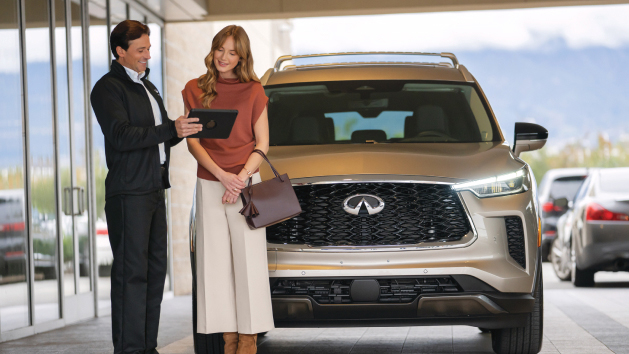 Woman standing beside man at an INFINITI Certified Pre-Owned Dealership with a certified used INFINITI QX60 in the background